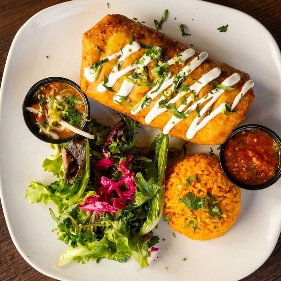 Golden-fried chimichanga drizzled with crema, served with rice, salad, and two dipping sauces.
