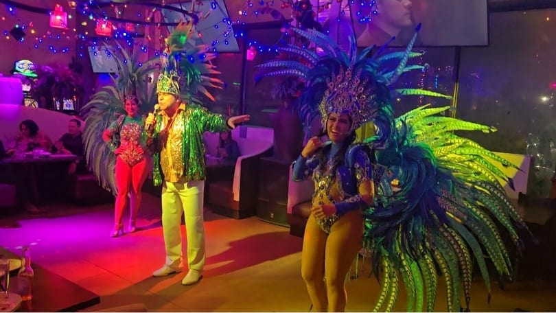 Performers in vibrant feathered costumes and a singer entertain guests in a lively restaurant.