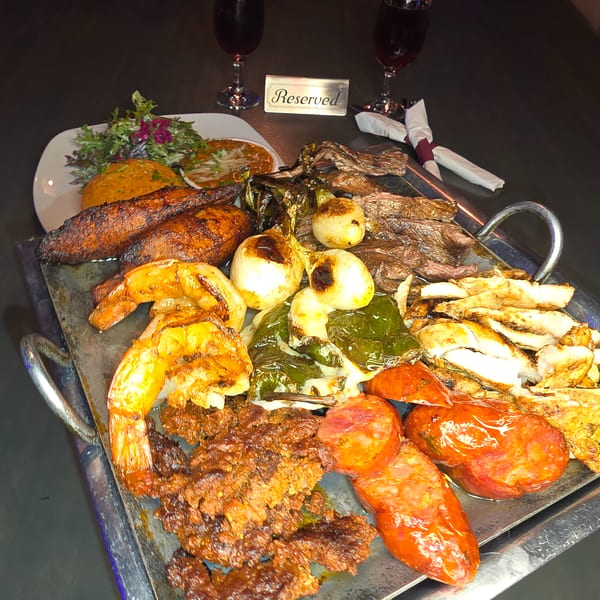 A large platter of grilled meats, shrimp, vegetables, and sides, with two wine glasses and a 'Reserved' sign.