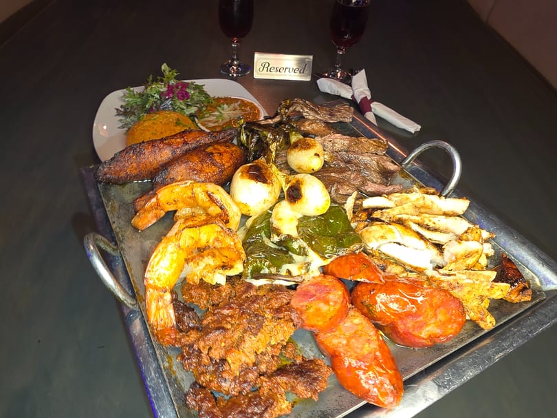 A large platter of grilled meats, shrimp, vegetables, and sides, with two wine glasses and a 'Reserved' sign.