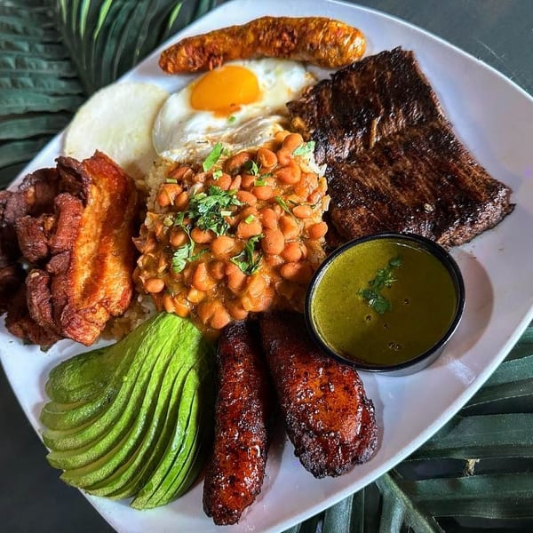 A large platter of Colombian bandeja paisa with steak, beans, rice, avocado, plantains, and fried egg.