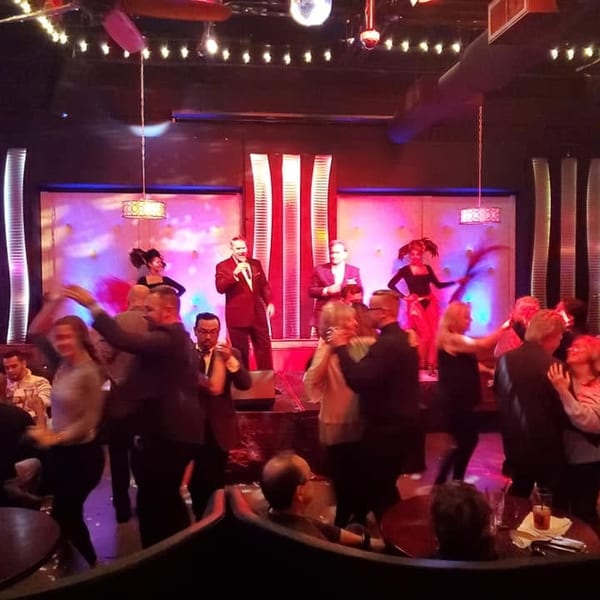 People dancing and enjoying live entertainment with a singer and dancers on stage.