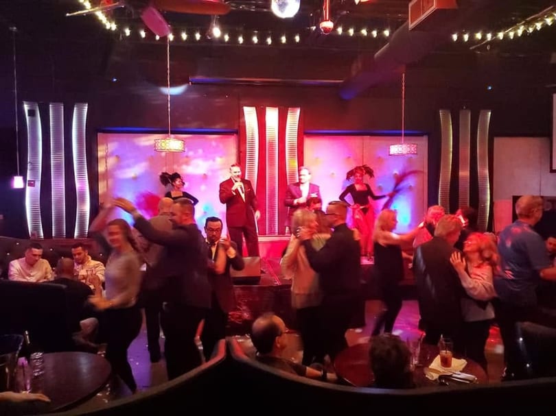 People dancing and enjoying live entertainment with a singer and dancers on stage.