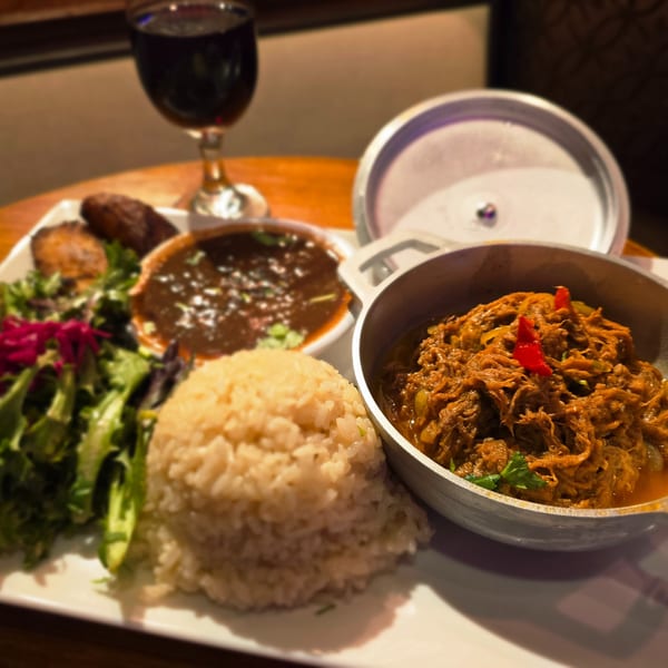 A plate of shredded meat, rice, salad, black beans, and plantains with a glass of red wine.