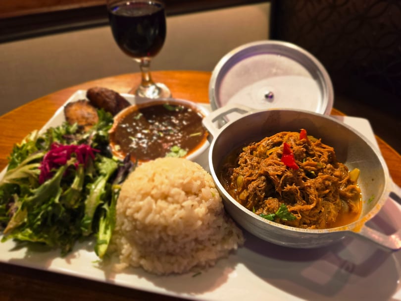 A plate of shredded meat, rice, salad, black beans, and plantains with a glass of red wine.