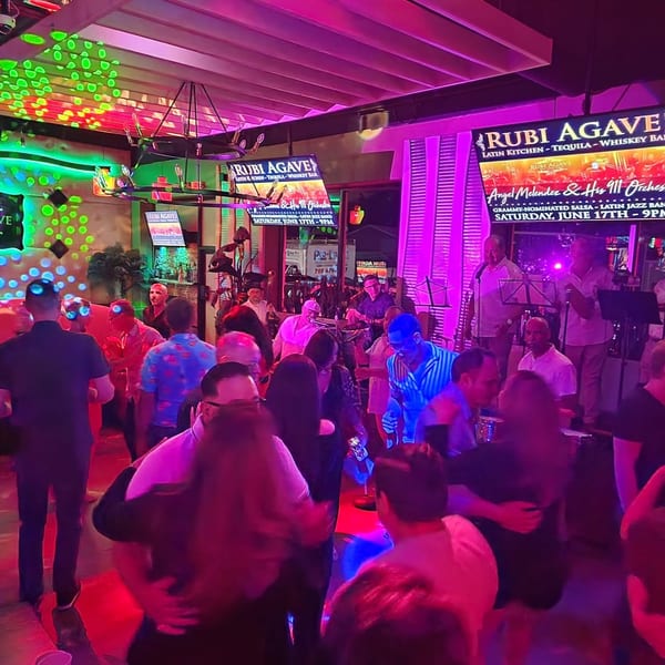 People dancing and enjoying live music under vibrant neon lights at Rubi Agave Latin Kitchen.